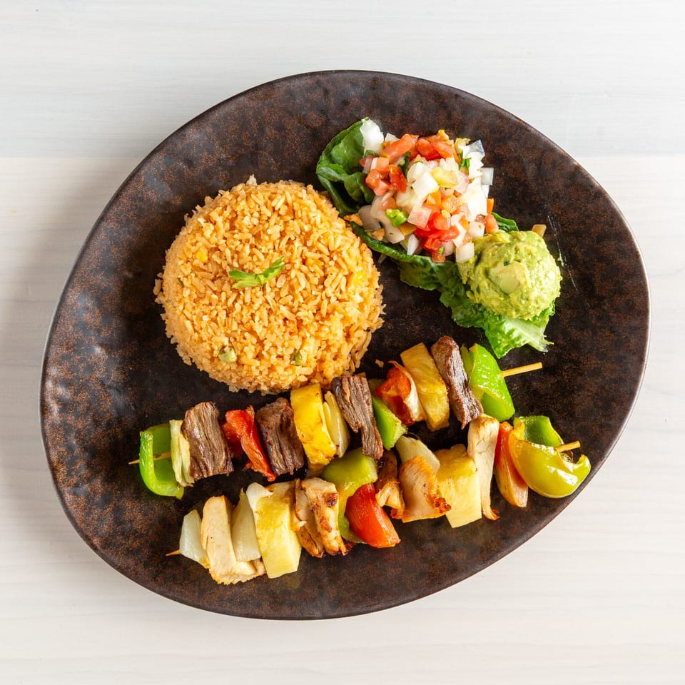 Grilled beef and chicken skewers with bell peppers, pineapple, rice, pico de gallo, and guacamole.