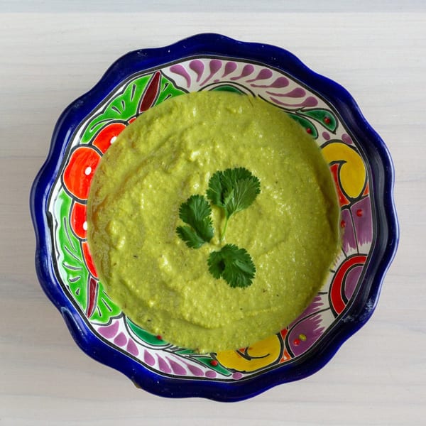 Bright green guacamole with cilantro in a colorful, scalloped blue bowl on a white surface.