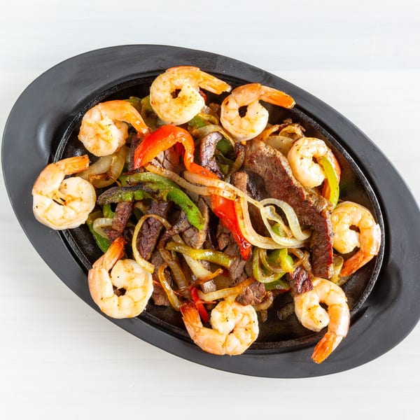 Sizzling shrimp and steak fajitas with colorful bell peppers and onions on a black platter.
