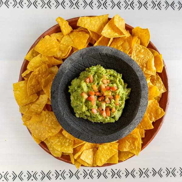 Overhead view of a molcajete filled with guacamole and diced tomatoes, surrounded by tortilla chips.