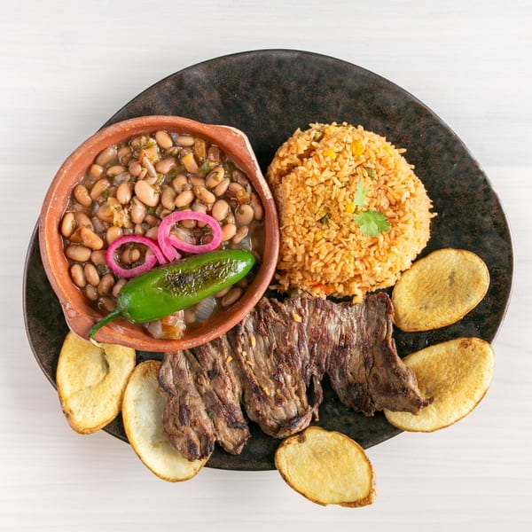 Grilled steak, rice, beans with pickled onions and a jalapeño, and potato slices on a dark plate.