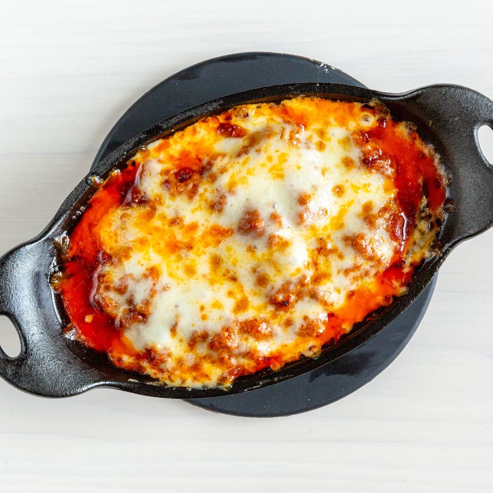 A bubbling cast iron dish of lasagna with melted cheese and rich red sauce on a white table.