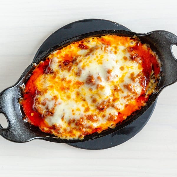 A bubbling hot cast iron dish filled with lasagna, topped with melted cheese and red sauce.