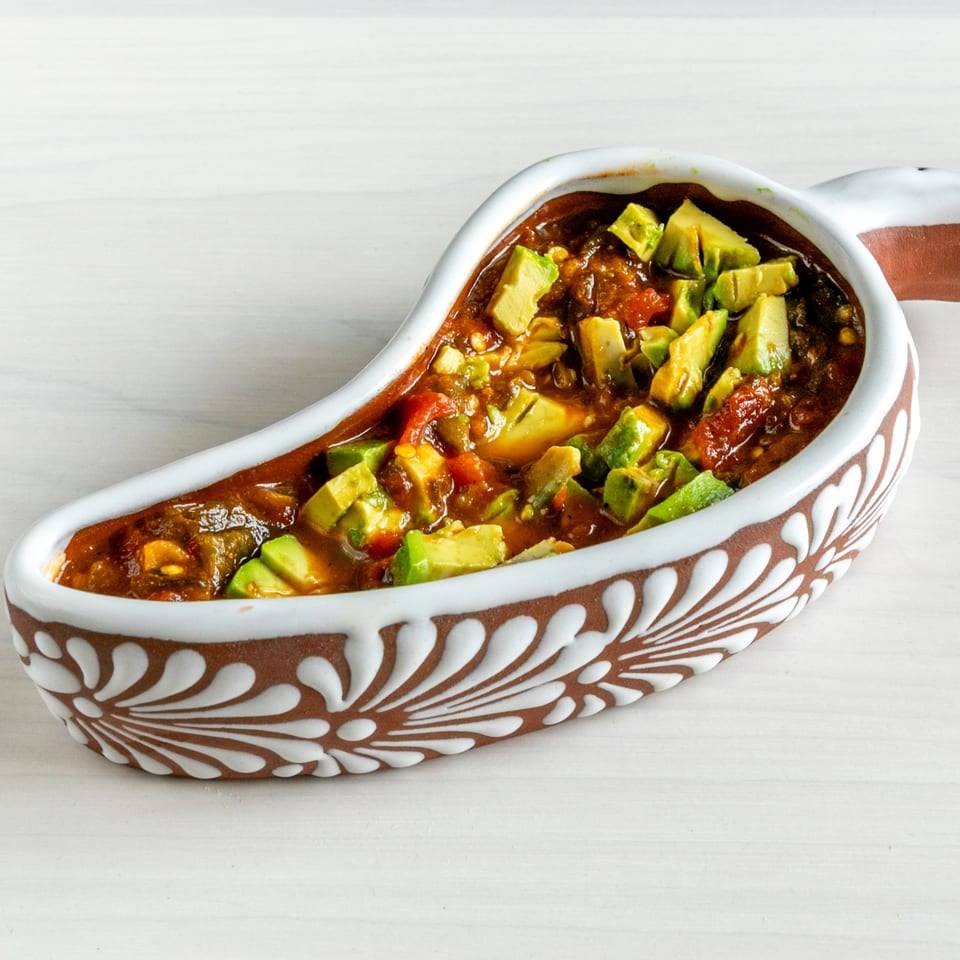 Chili with diced avocado in a chili-shaped bowl with white and brown patterns.