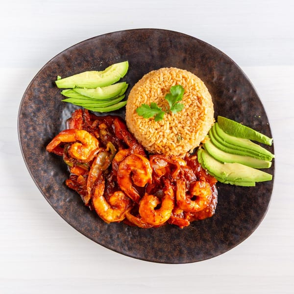 Spicy shrimp with red sauce, rice, and sliced avocado on a dark plate.