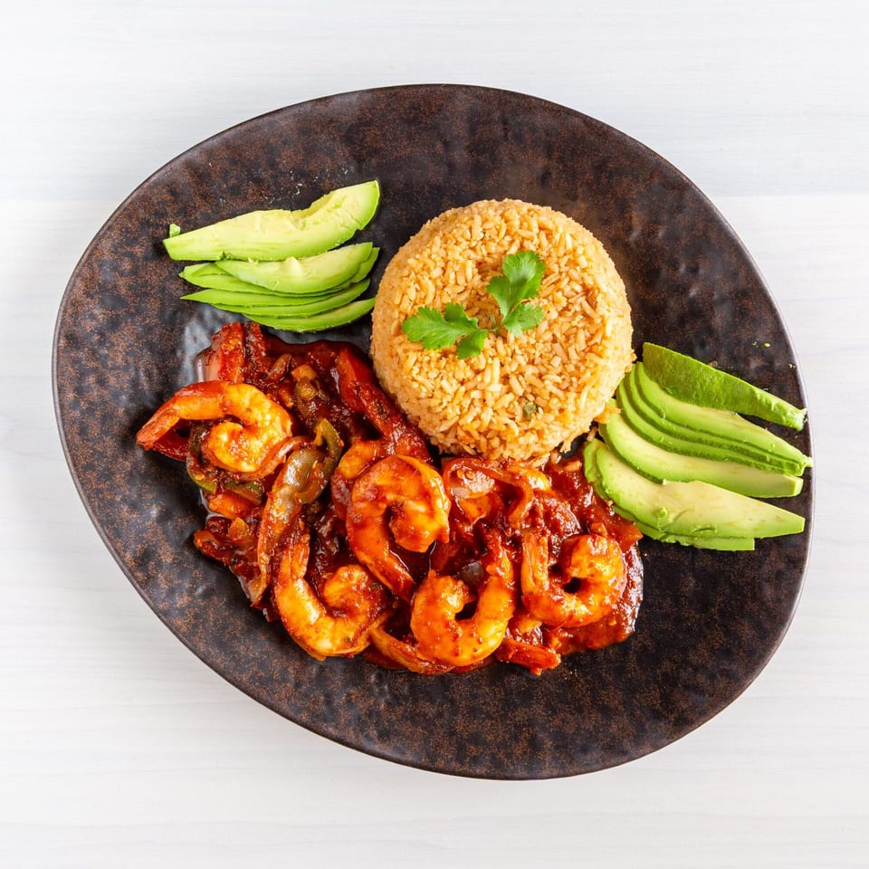 Spicy shrimp with red sauce, rice, and sliced avocado on a dark plate.